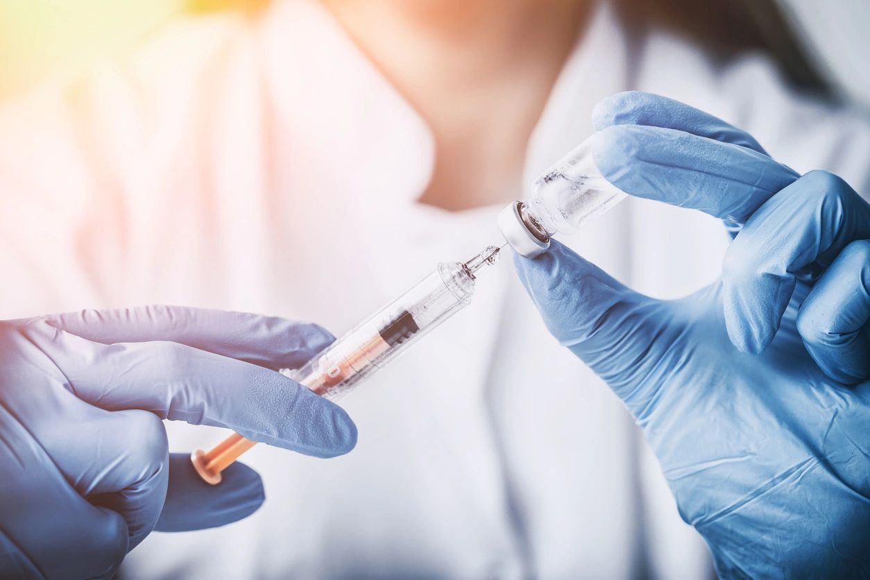 hands in blue medical gloves holding a syringe and drawing from a vile